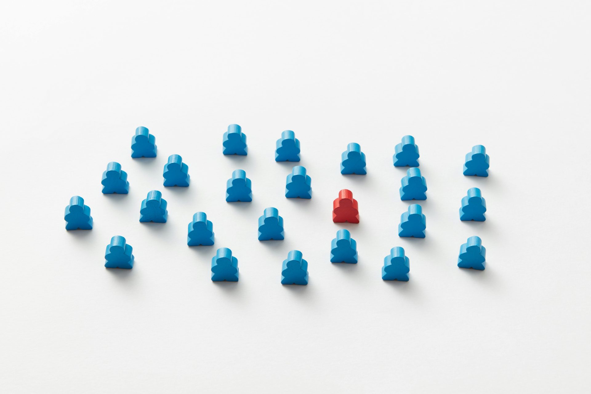A red meeple stands out in a pattern of blue figures, symbolizing individuality.
